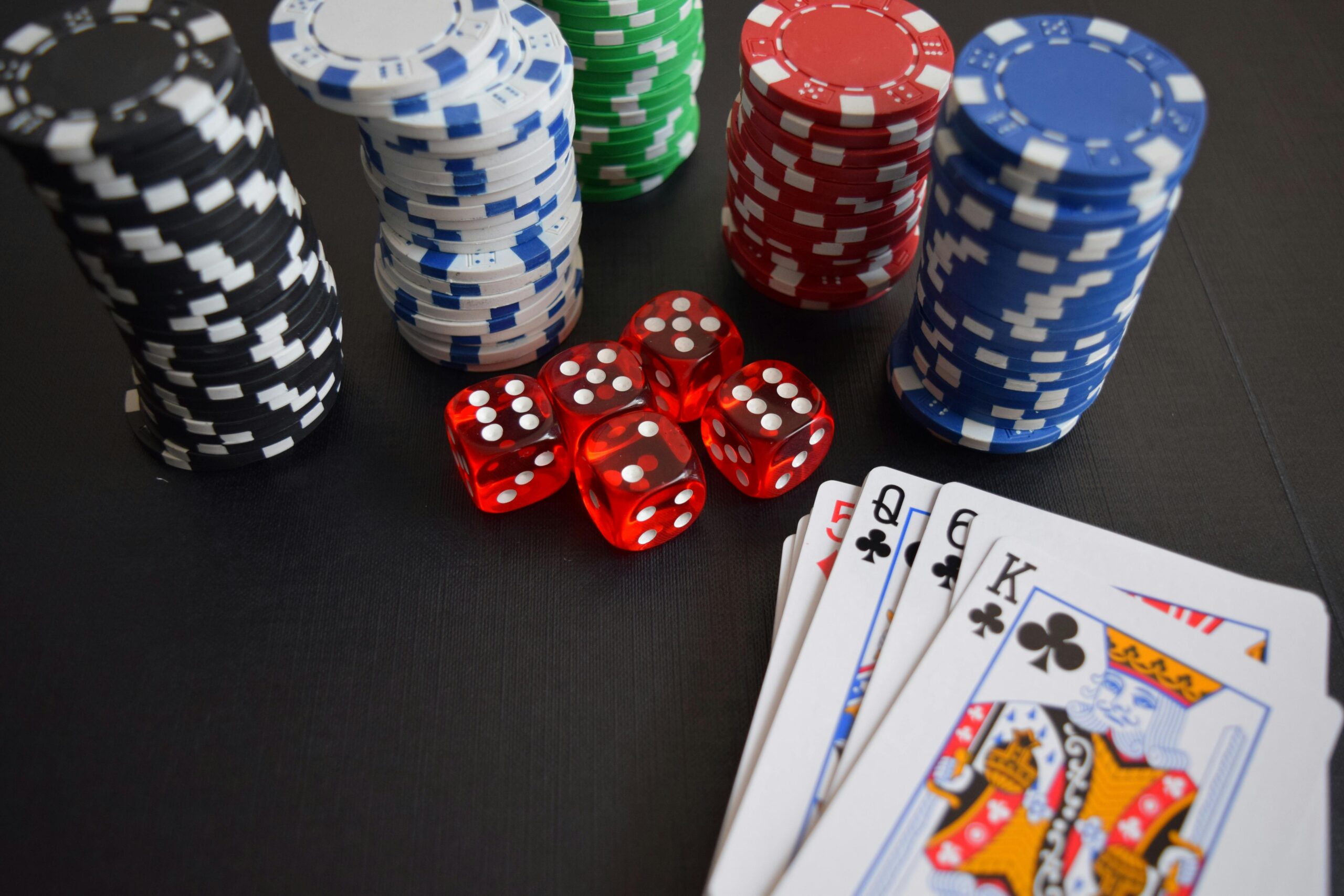 Mehrere Stapel verschiedenfarbiger Pokerchips, rote Würfel sowie einem Stapel Pokerkarten.
